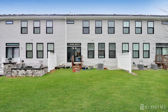 rear view of property with entry steps, a lawn, and cooling unit