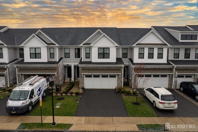 view of property with board and batten siding, an attached garage, stone siding, driveway, and a front lawn