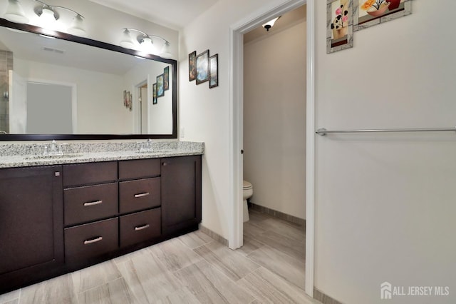 full bath featuring toilet, double vanity, and baseboards