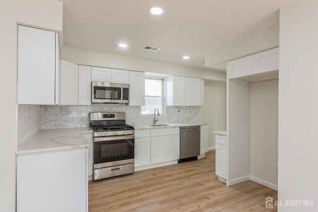 17-1/2 Thomas St, South River, NJ 08882 - kitchen featuring stainless steel appliances, white cabinetry, backsplash, light stone counters, and light wood finished floors