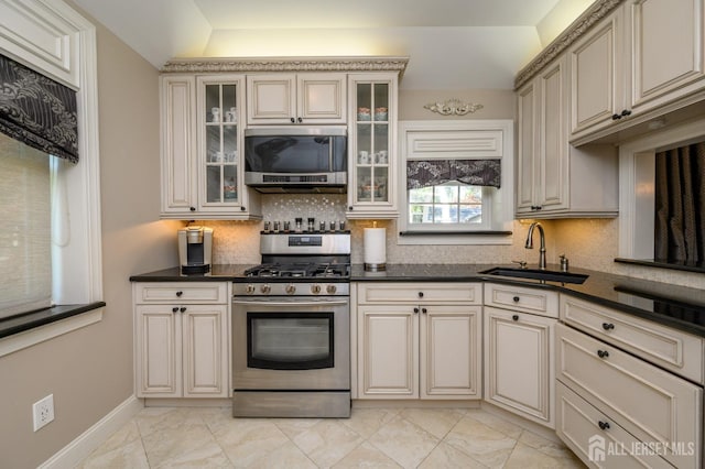 kitchen featuring marble finish floor, dark countertops, cream cabinets, a sink, and appliances with stainless steel finishes