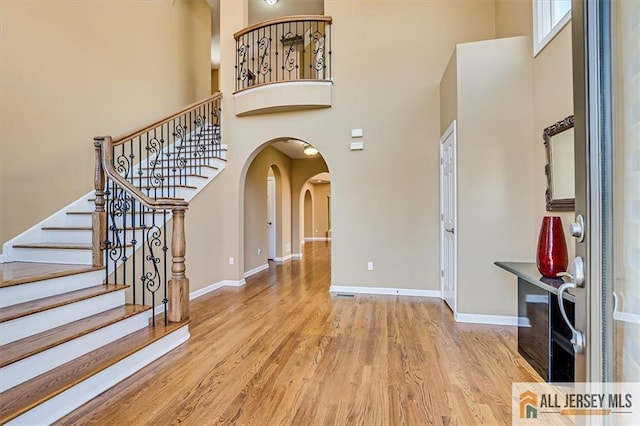 entryway with baseboards, arched walkways, wood finished floors, and a towering ceiling