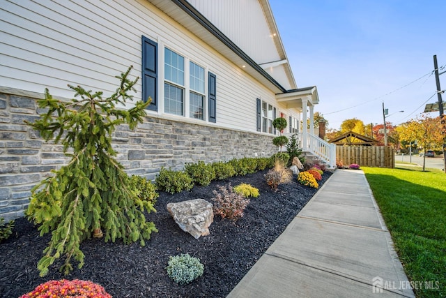 view of side of property with a yard, stone siding, and fence