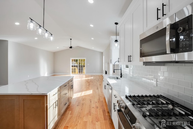 kitchen featuring lofted ceiling, light wood finished floors, a sink, backsplash, and stainless steel appliances