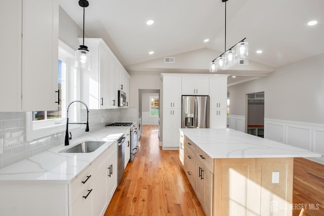 kitchen featuring a kitchen island, a sink, visible vents, appliances with stainless steel finishes, and vaulted ceiling