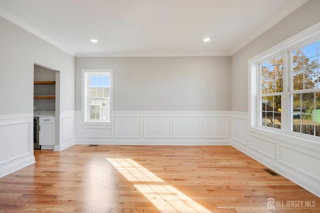 spare room with a wainscoted wall, light wood-style floors, visible vents, and ornamental molding