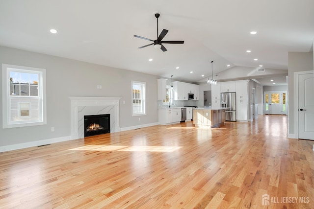 unfurnished living room featuring visible vents, ceiling fan, a sink, a high end fireplace, and vaulted ceiling