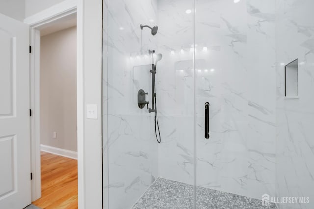 bathroom with a marble finish shower, baseboards, and wood finished floors