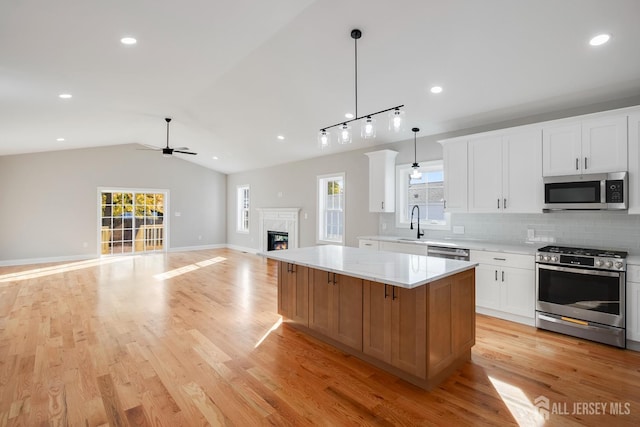 kitchen featuring a center island, a ceiling fan, a premium fireplace, backsplash, and appliances with stainless steel finishes