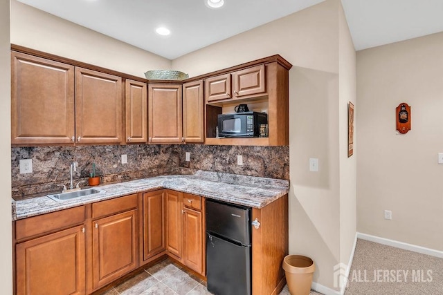kitchen featuring light stone countertops, black appliances, decorative backsplash, and a sink