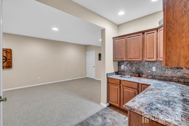 kitchen with a sink, brown cabinetry, light carpet, backsplash, and baseboards