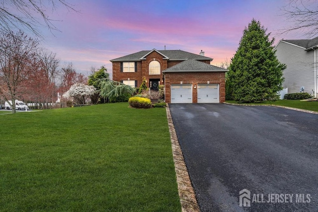 traditional-style home featuring a chimney, aphalt driveway, an attached garage, a front yard, and brick siding