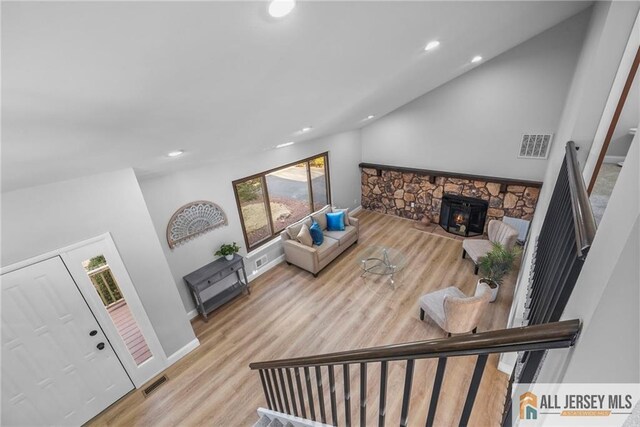 living room featuring a wood stove, light hardwood / wood-style flooring, and high vaulted ceiling