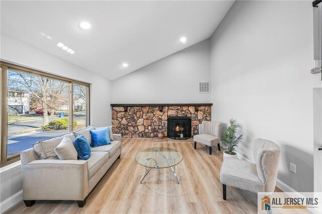 living room with plenty of natural light, light hardwood / wood-style floors, a stone fireplace, and lofted ceiling