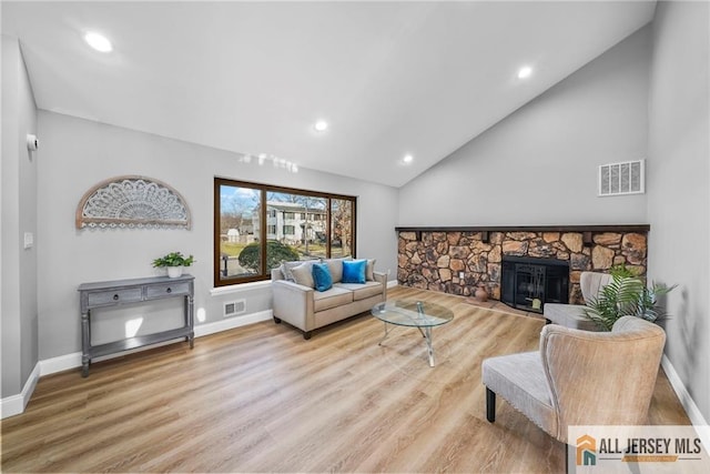 living room featuring high vaulted ceiling, light hardwood / wood-style floors, and a stone fireplace