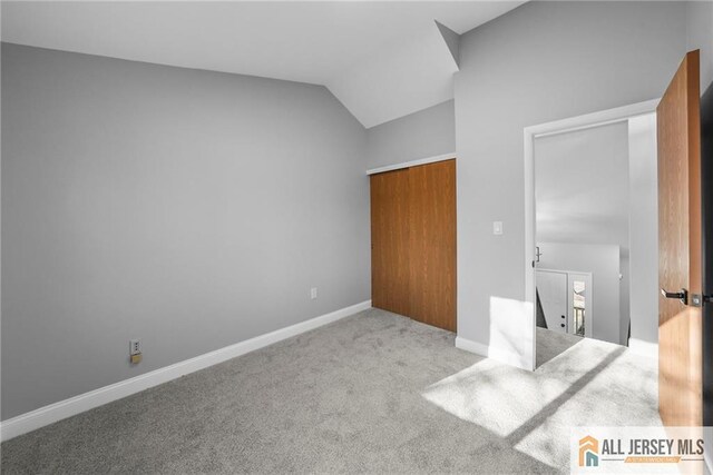 unfurnished bedroom with a closet, light carpet, and vaulted ceiling