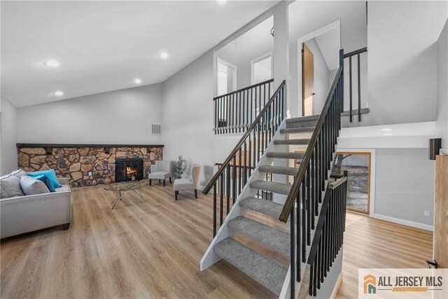 stairs with hardwood / wood-style flooring, a fireplace, and high vaulted ceiling