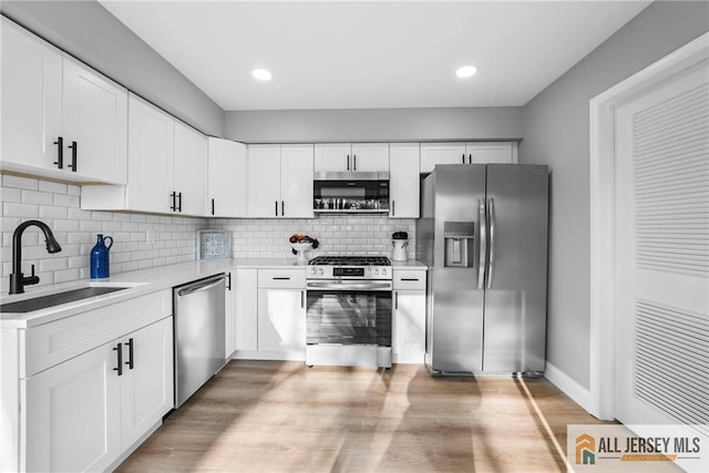 kitchen featuring sink, light hardwood / wood-style flooring, decorative backsplash, white cabinets, and appliances with stainless steel finishes