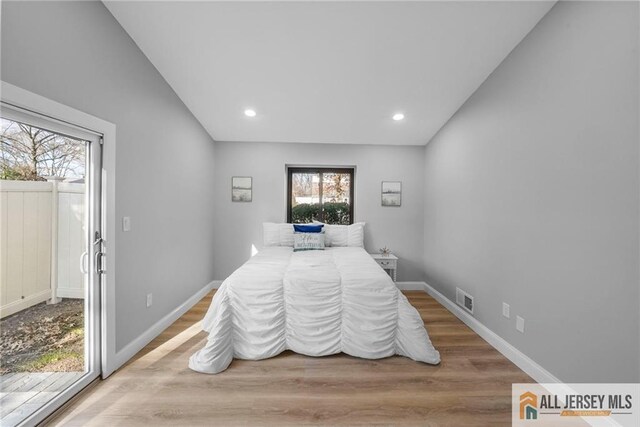 bedroom featuring access to exterior, vaulted ceiling, light hardwood / wood-style flooring, and multiple windows