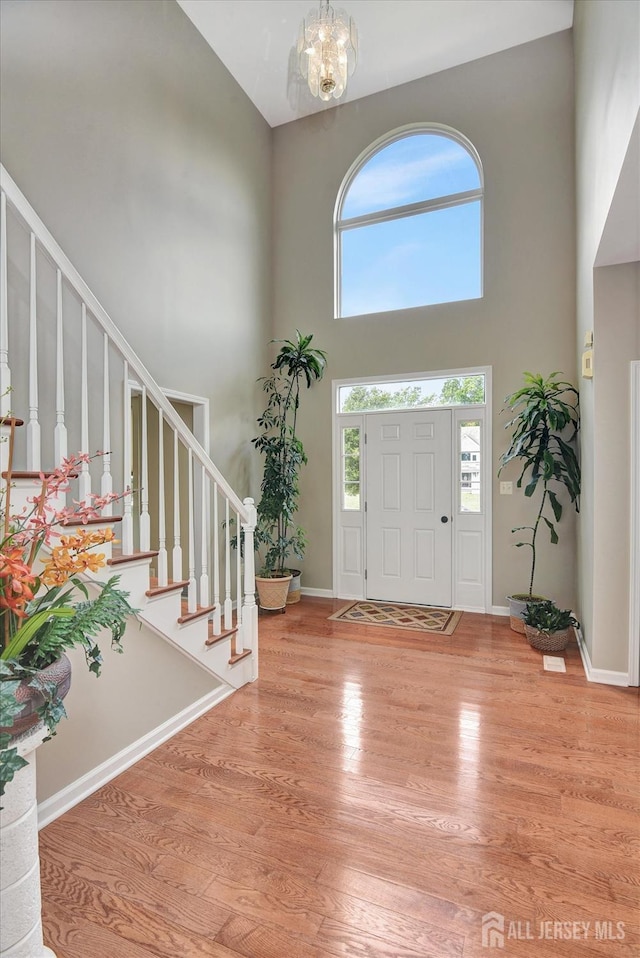 entryway featuring light wood-type flooring, a towering ceiling, and a chandelier