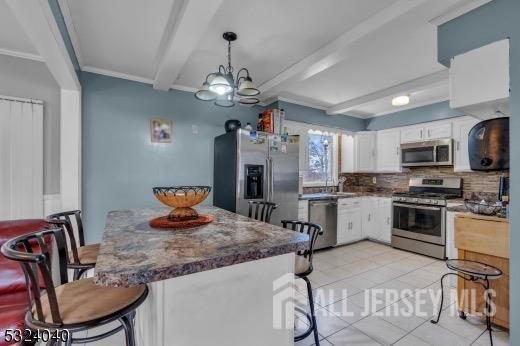27 6th Ave, Port Reading, NJ 07064 - kitchen with appliances with stainless steel finishes, white cabinetry, beam ceiling, decorative backsplash, and a breakfast bar