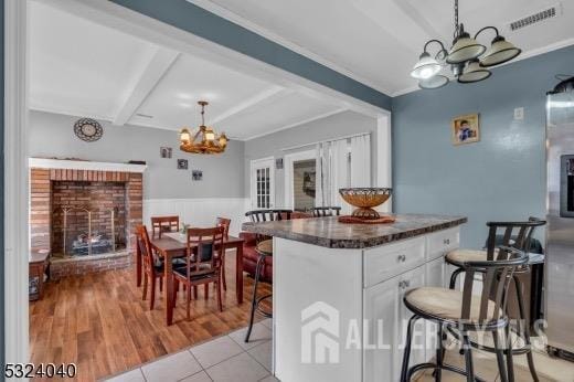 27 6th Ave, Port Reading, NJ 07064 - kitchen with a chandelier, a brick fireplace, white cabinets, beam ceiling, and hanging light fixtures