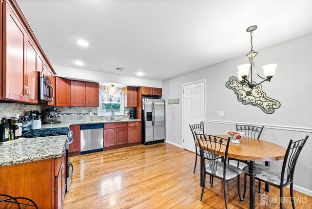kitchen featuring appliances with stainless steel finishes, an inviting chandelier, light wood finished floors, decorative backsplash, and visible vents