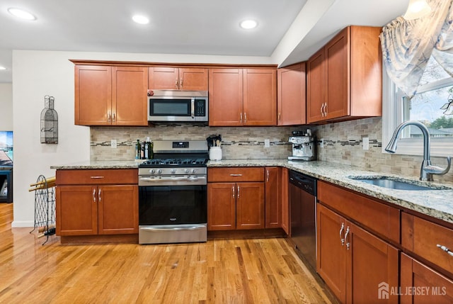 kitchen with light stone counters, a sink, light wood-style flooring, and appliances with stainless steel finishes