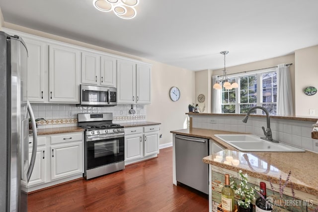 kitchen featuring hanging light fixtures, dark wood-type flooring, stainless steel appliances, white cabinets, and sink