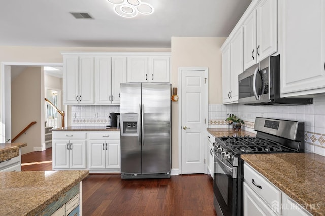 kitchen featuring white cabinetry, dark stone countertops, dark hardwood / wood-style flooring, appliances with stainless steel finishes, and decorative backsplash