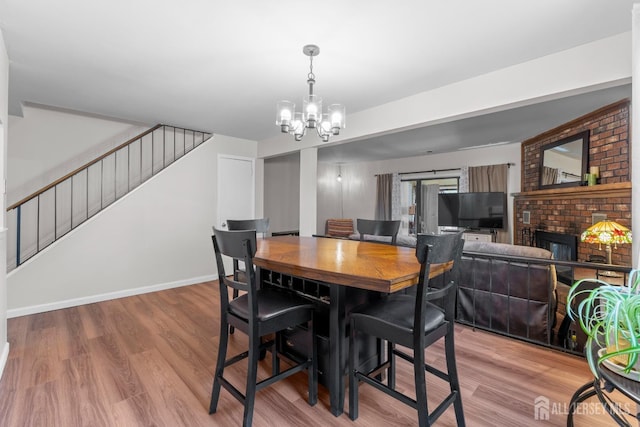 dining space featuring baseboards, wood finished floors, an inviting chandelier, stairs, and a fireplace