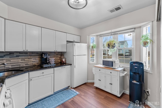 kitchen featuring white appliances, wood finished floors, a sink, visible vents, and backsplash