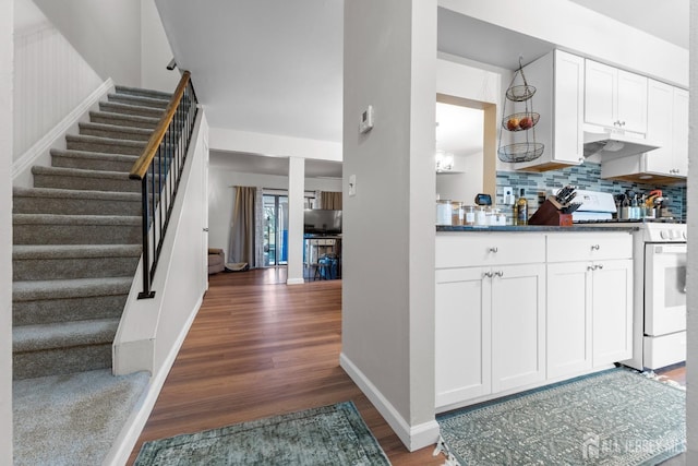 kitchen with white range with gas stovetop, white cabinets, wood finished floors, under cabinet range hood, and backsplash