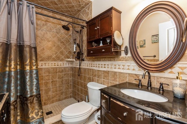 bathroom featuring tile walls, a wainscoted wall, a tile shower, toilet, and vanity