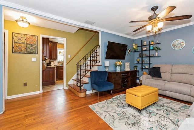 living room featuring ceiling fan, crown molding, stairway, and light wood-type flooring