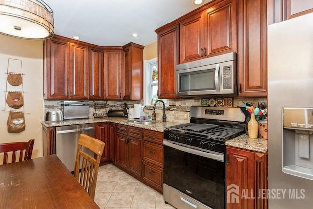 kitchen featuring light stone countertops, stainless steel appliances, a sink, backsplash, and light tile patterned floors