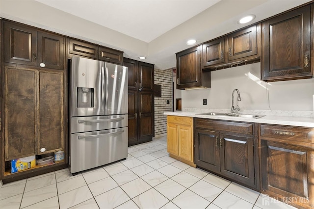 kitchen featuring sink, dark brown cabinetry, stainless steel refrigerator with ice dispenser, and brick wall