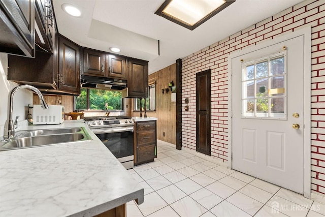 kitchen featuring brick wall, dark brown cabinets, sink, light tile patterned floors, and stainless steel range oven