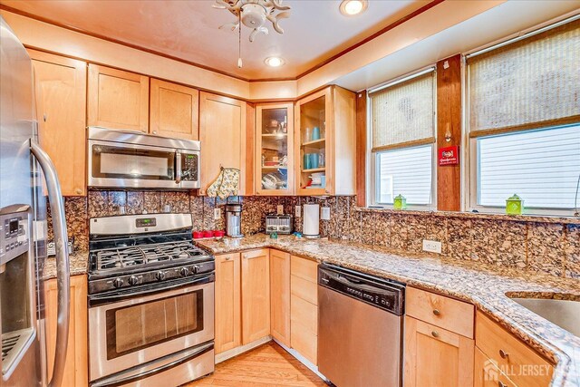 kitchen with light hardwood / wood-style flooring, stainless steel appliances, tasteful backsplash, light stone countertops, and light brown cabinets