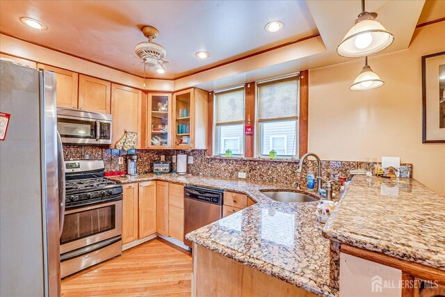 kitchen featuring appliances with stainless steel finishes, pendant lighting, sink, kitchen peninsula, and light stone countertops