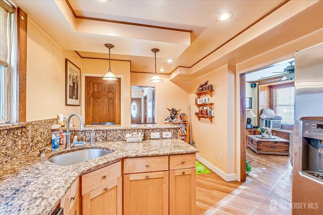 kitchen featuring sink, decorative light fixtures, light brown cabinets, light wood-type flooring, and a tray ceiling