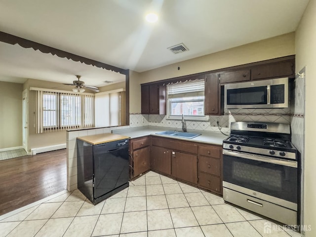 kitchen featuring sink, baseboard heating, decorative backsplash, light tile patterned flooring, and appliances with stainless steel finishes