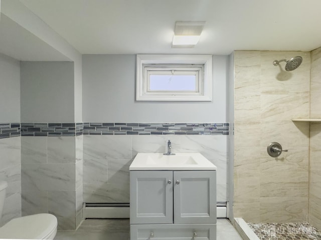 bathroom with vanity, baseboard heating, tiled shower, tile walls, and toilet