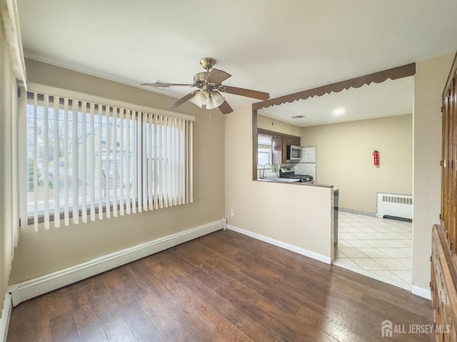 empty room with ceiling fan, wood-type flooring, radiator heating unit, and a baseboard heating unit