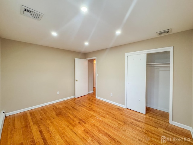 unfurnished bedroom featuring light wood-type flooring, a baseboard radiator, and a closet