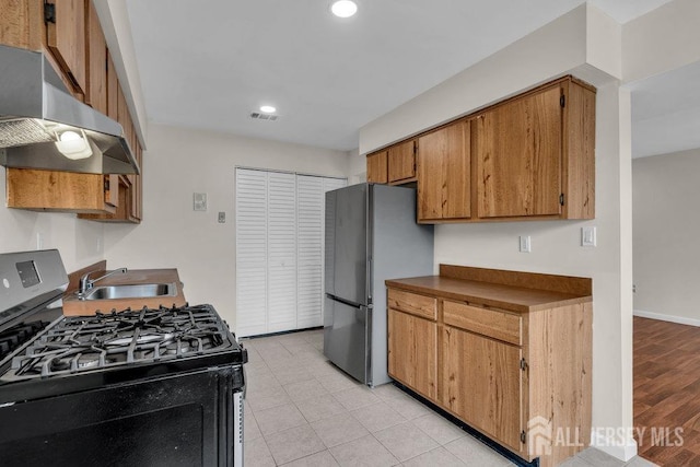 kitchen featuring range with gas stovetop, brown cabinets, freestanding refrigerator, a sink, and under cabinet range hood