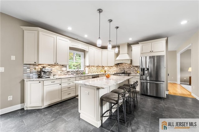 kitchen with light stone countertops, premium range hood, pendant lighting, a kitchen island, and appliances with stainless steel finishes