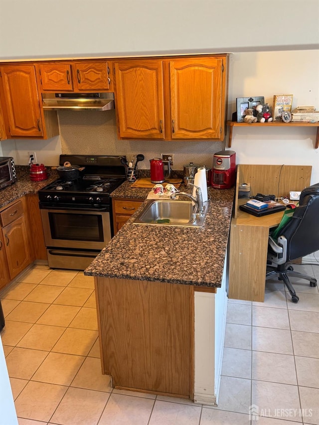 kitchen with brown cabinets, under cabinet range hood, a sink, light tile patterned floors, and stainless steel range with gas stovetop