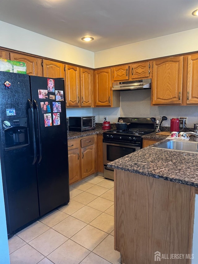 kitchen with under cabinet range hood, a sink, appliances with stainless steel finishes, brown cabinetry, and light tile patterned floors