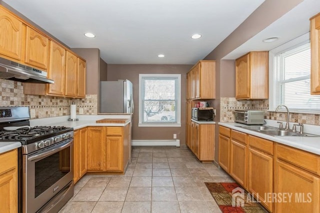 kitchen with a sink, under cabinet range hood, stainless steel appliances, light countertops, and baseboard heating